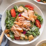 Bowl of salmon kale Caesar salad with tomatoes, Parmesan, and croutons.