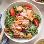 Bowl of salmon kale Caesar salad with tomatoes, Parmesan, and croutons.