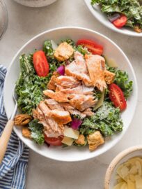 Bowl of salmon kale Caesar salad with tomatoes, Parmesan, and croutons.