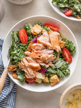 Bowl of salmon kale Caesar salad with tomatoes, Parmesan, and croutons.
