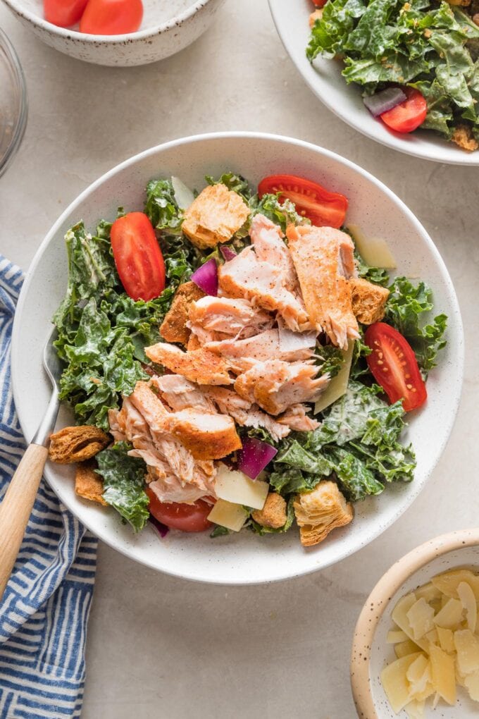 Bowl of salmon kale Caesar salad with tomatoes, Parmesan, and croutons.