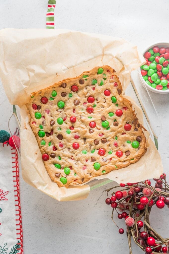 Square baking pan lined with parchment and holding a batch of holiday M&M blondies.