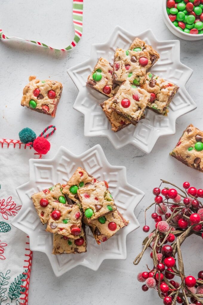 Countertop scattered with holiday ribbon, ornaments, and two plates of Christmas blondies decorated with red and green M&Ms.