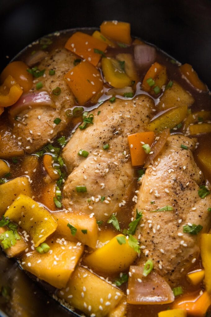 Close up of slow cooker pineapple chicken garnished with green onions and sesame seeds inside the Crockpot.