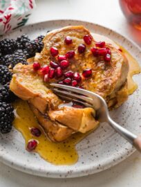 Close up of a fork pulling off bites of eggnog French toast from a stack of slices on a small plate.