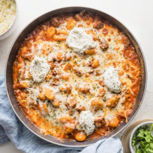 Overhead view of a pan full of ground beef baked gnocchi with a creamy tomato sauce, mozzarella and ricotta cheese, and a bit of fresh parsley.