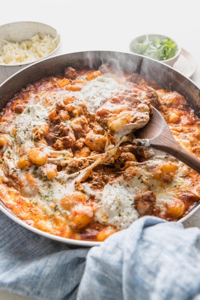 A spoon lifting out a still-steaming portion of ground beef baked gnocchi from a skillet.