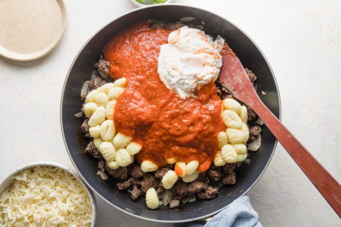 Dried gnocchi, marinara sauce, seasoning, and ricotta cheese added to browned ground beef in a skillet.