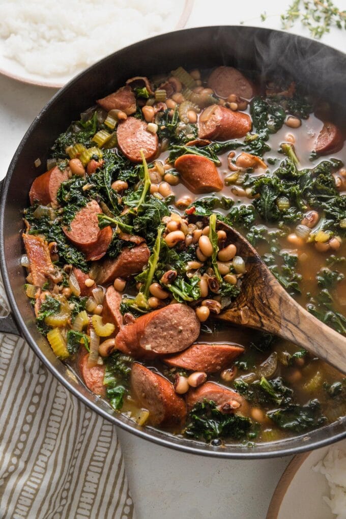 Close up of a serving spoon stirring a portion of Hoppin' John in a large cast iron skillet.