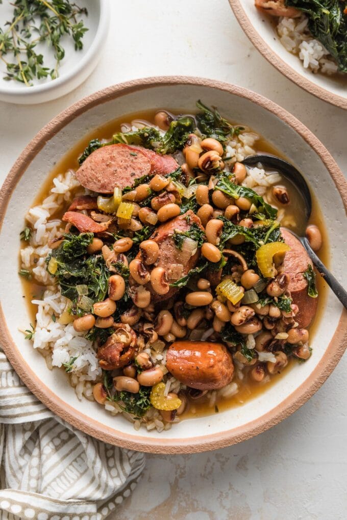 Small bowl with a portion of black eyed pea stew served over white rice and garnished with sprigs of fresh thyme.