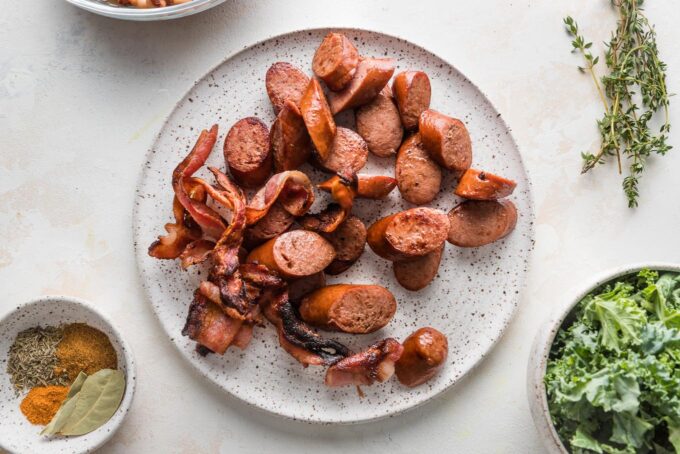 Brown turkey smoked sausage and crisped slices of bacon resting together on a small white plate.