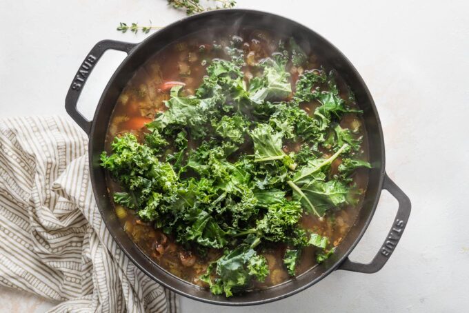 Kale being stirred straight into a black eyed pea recipe being made with broth in a large deep skillet.