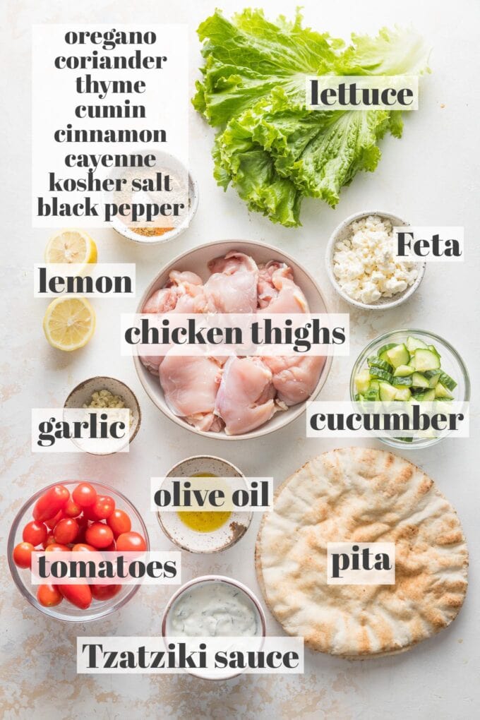 Labeled overhead photo of boneless, skinless chicken thighs; pita, lettuce, tomatoes, Feta, Tzatziki sauce, olive oil, minced garlic, lemon, and a spice blend of oregano, coriander, thyme, cumin, cinnamon, cayenne, kosher salt, and black pepper, all measured into prep bowls and ready to cook and assemble into gyros.