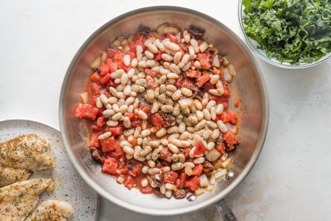 Cannellini beans and diced tomatoes with seasoning in a skillet.