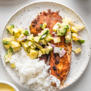 Small white plate with a serving of blackened fish topped with mango avocado salsa and white rice on the side.