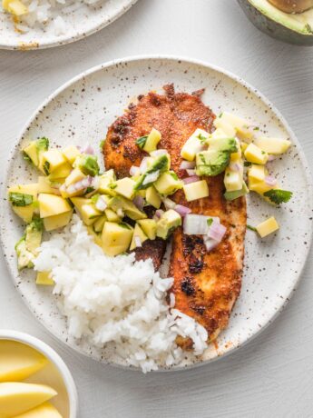 Small white plate with a serving of blackened fish topped with mango avocado salsa and white rice on the side.