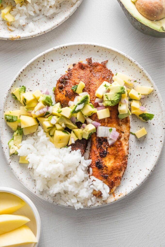Small white plate with a serving of blackened fish topped with mango avocado salsa and white rice on the side.