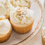 Close up angled view of a champagne cupcake decorated with champagne buttercream piped on in different designs and topped with gold and white assorted sprinkles.