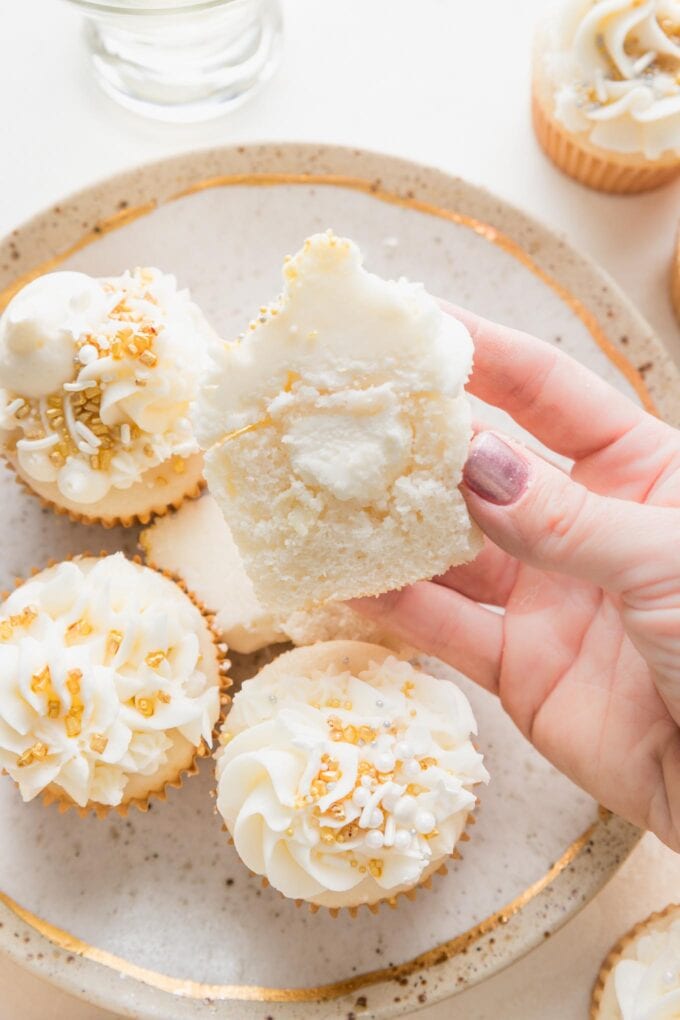 Close up of a hand holding up half of a champagne cupcake , cut open to reveal that the inside is filled with extra champagne-flavored buttercream.