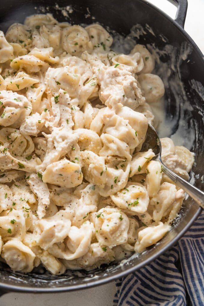 Close up of a serving spoon lifting a portion of chicken tortellini Alfredo out of a skillet.