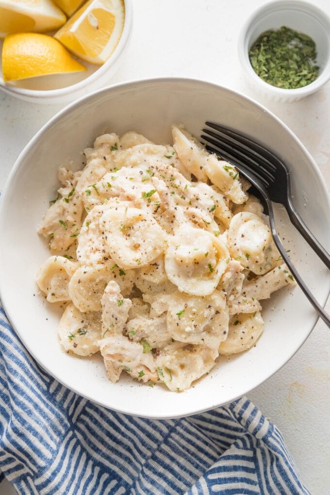 Small white bowl holding a big portion of creamy, cheesy chicken tortellini Alfredo.