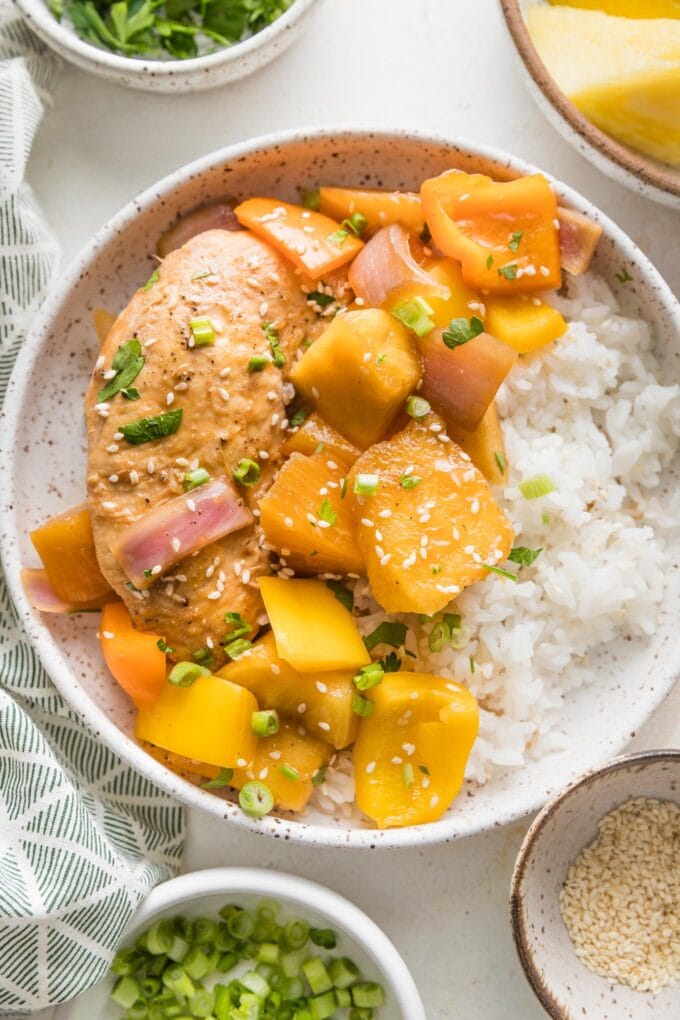 Bowl full of slow cooker pineapple chicken served with white rice, green onions, and sesame seeds.
