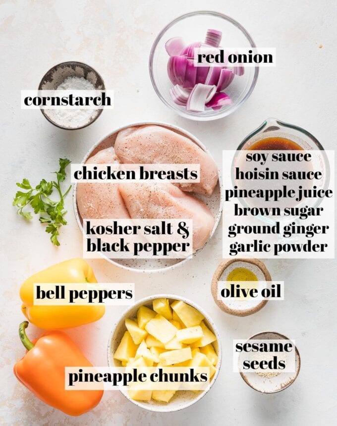 Labeled overhead photo of chicken breasts seasoned with salt and pepper, red onion, bell peppers, pineapple chunks, olive oil, cornstarch, sesame seeds, and a measuring cup filled with soy sauce, hoisin sauce, pineapple juice, brown sugar, ground ginger, and garlic powder, all measured and ready to cook.