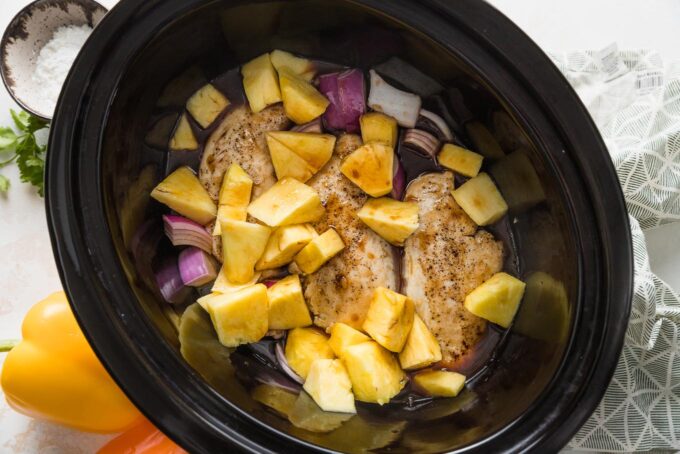 Sauce poured over pineapple chicken in a Crockpot, ready to cook.