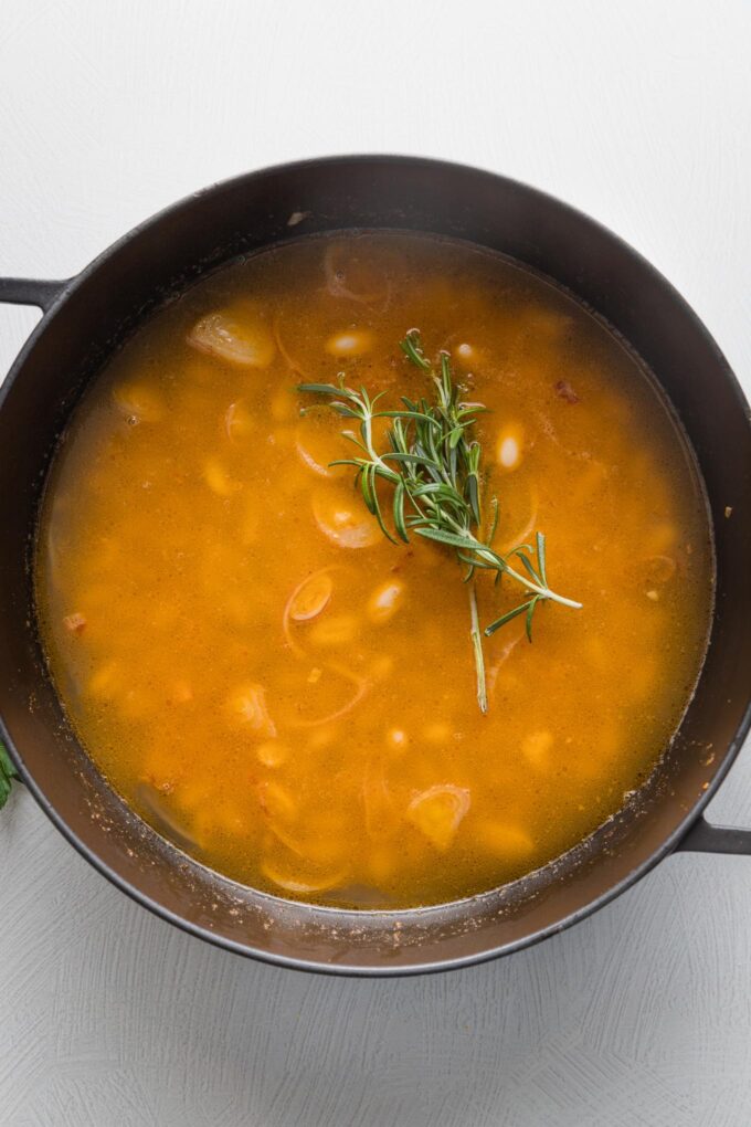 Rich orange broth simmering with sprigs of rosemary.