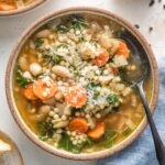 Small bowl full of Crockpot white bean soup with Parmesan and pearl couscous, with extra Parmesan grated on top as a garnish.