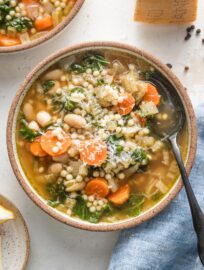 Small bowl full of Crockpot white bean soup with Parmesan and pearl couscous, with extra Parmesan grated on top as a garnish.