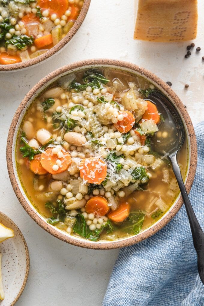 Small bowl full of Crockpot white bean soup with Parmesan and pearl couscous, with extra Parmesan grated on top as a garnish.