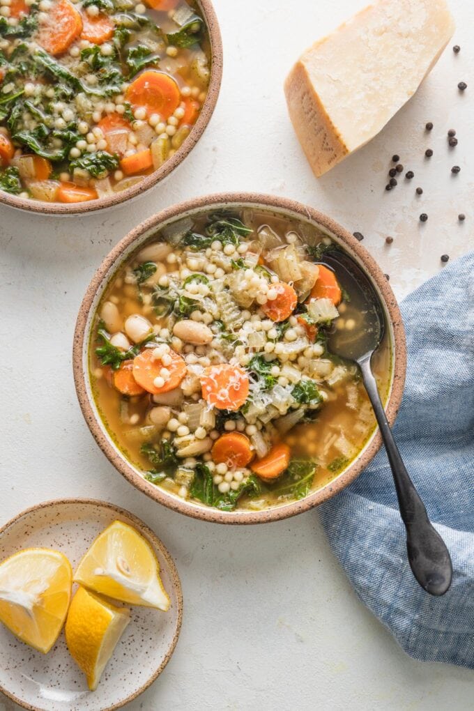 Table filled with two bowls of slow cooker white bean soup garnished with lemon wedges and grated Parmesan cheese.