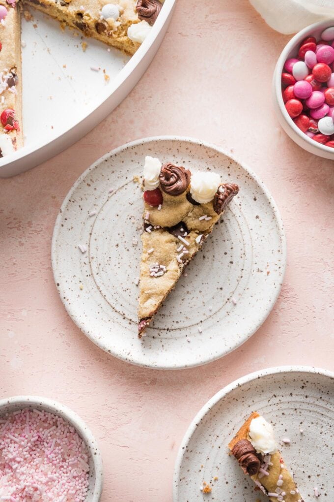 Pink countertop set with small dessert plates holding slices of a heart-shaped chocolate chip cookie cake.