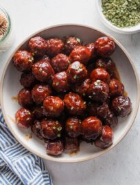 Shallow ceramic bowl filled with sweet and sticky crockpot BBQ meatballs, garnished with chives and ready to serve.