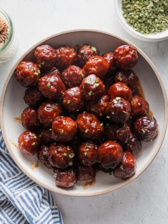 Shallow ceramic bowl filled with sweet and sticky crockpot BBQ meatballs, garnished with chives and ready to serve.