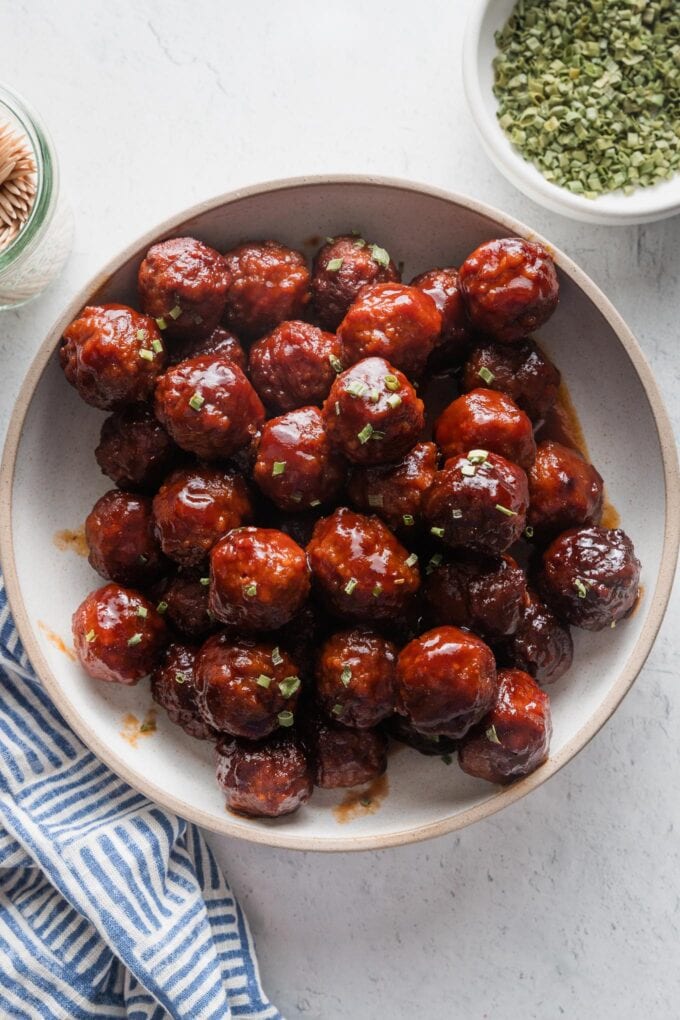 Shallow ceramic bowl filled with sweet and sticky crockpot BBQ meatballs, garnished with chives and ready to serve.