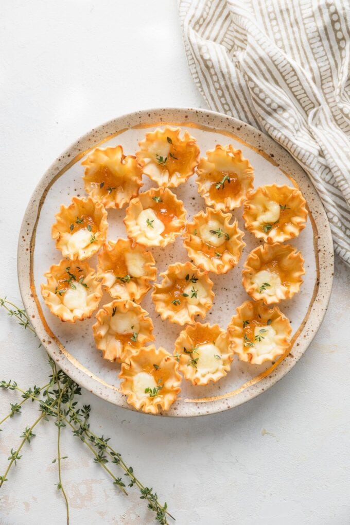 Overhead view of a countertop with a decorative napkin, sprigs of fresh thyme, and a plate of apricot brie bite appetizers.