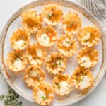 Gold-rimmed speckled plate holding apricot brie phyllo cups garnished with fresh thyme leaves.