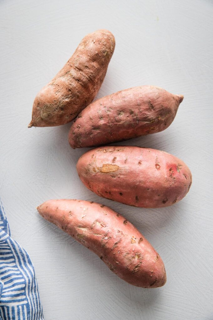 Four sweet potatoes laid out on a countertop.