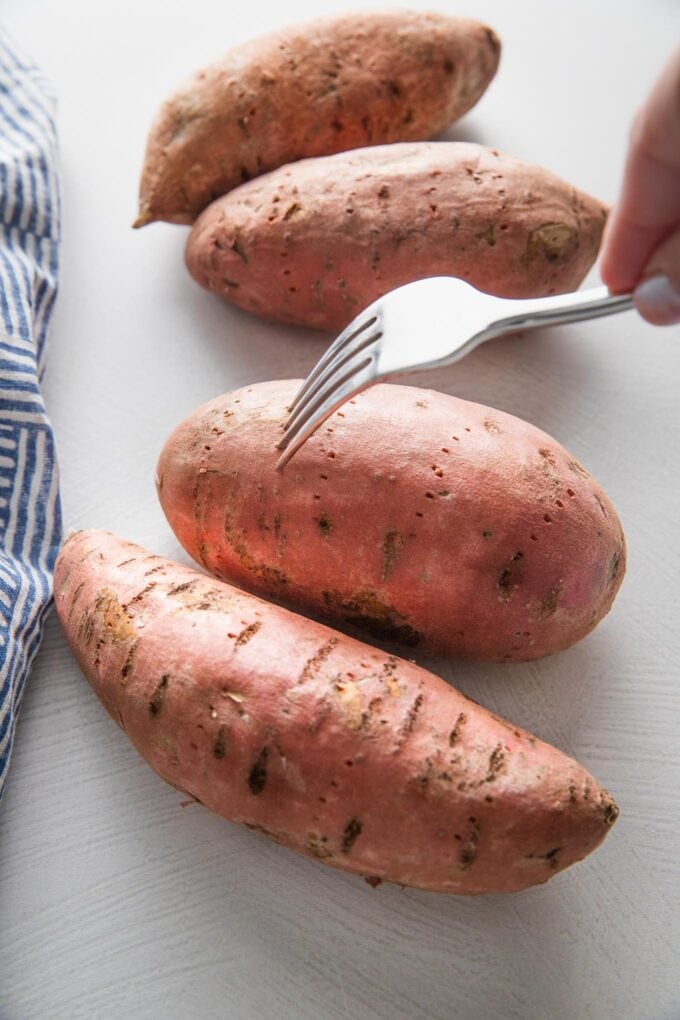 Fork pricking a sweet potato with holes.