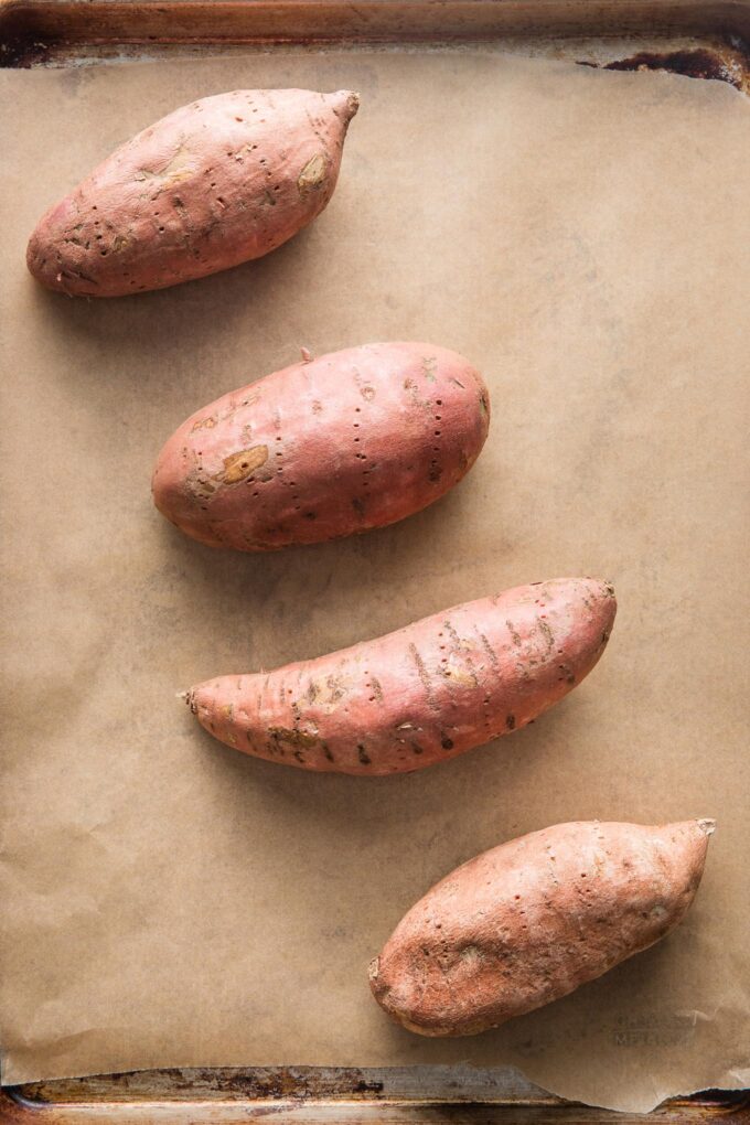 Sweet potatoes laid out on a parchment-lined baking sheet.