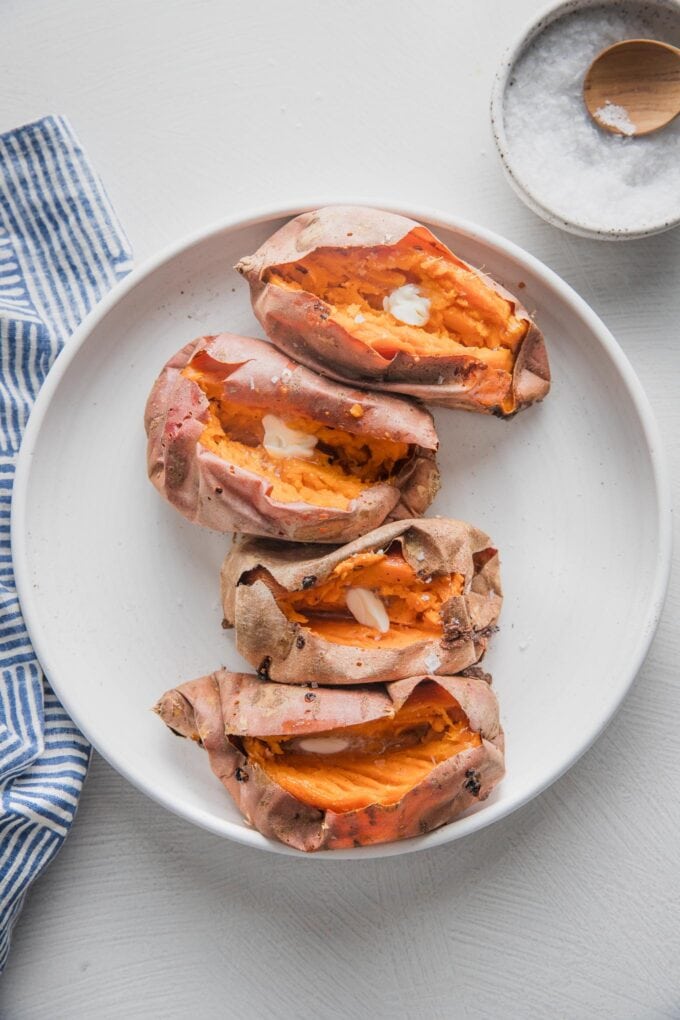 White platter holding four baked sweet potatoes.