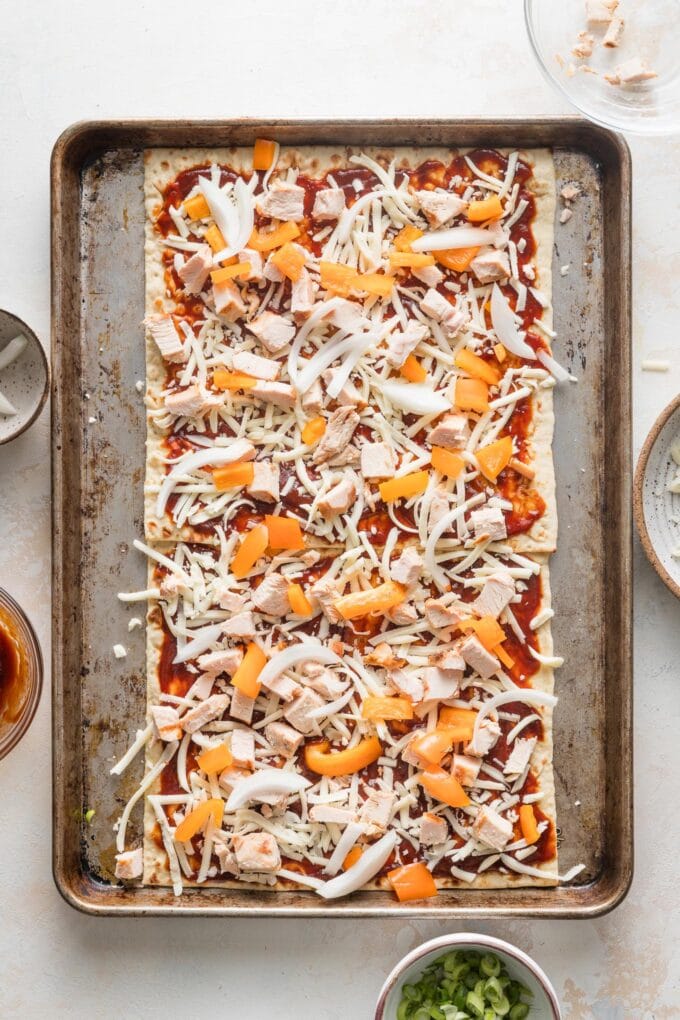 Shredded mozzarella cheese, chicken, peppers, and onions spread out on flatbread and ready to bake.
