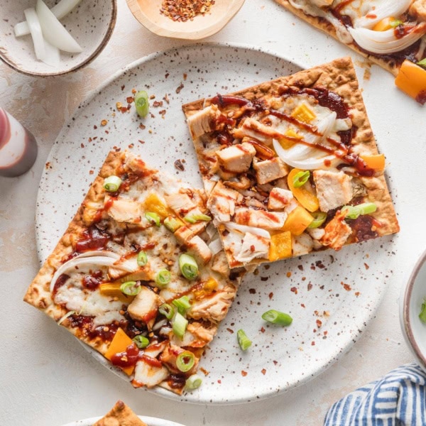 Small white plate with two pieces of BBQ chicken flatbread garnished with green onion and red pepper flakes.