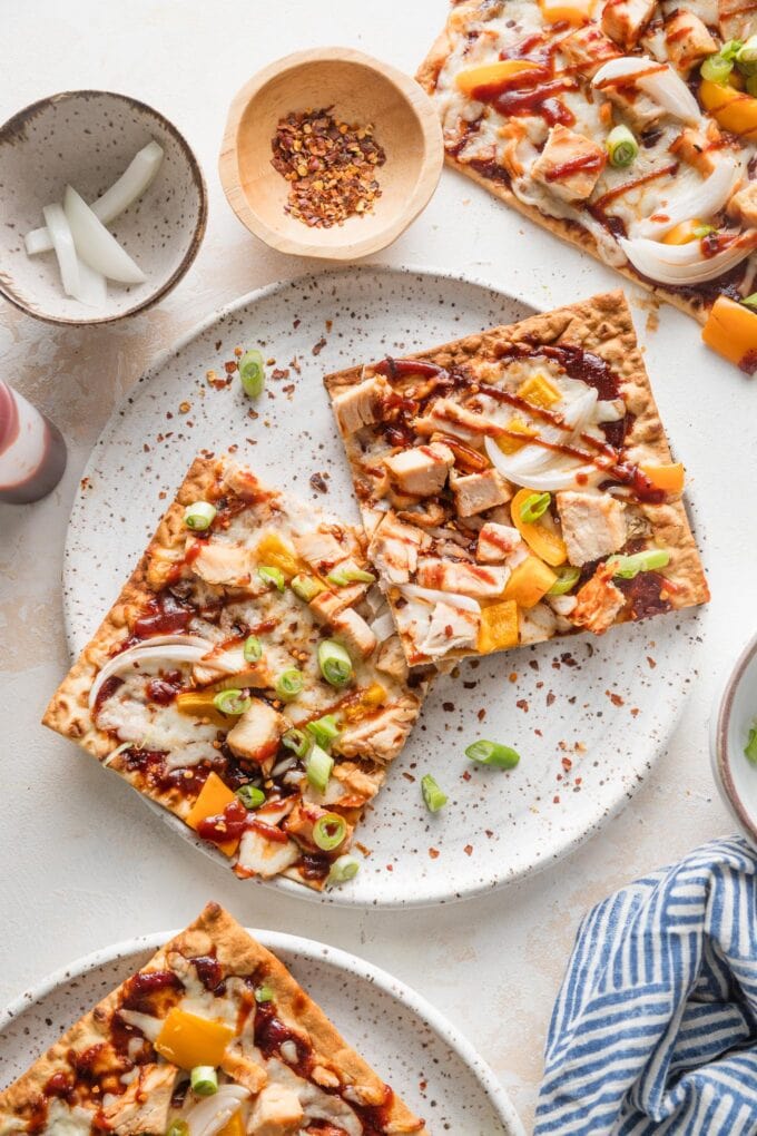 Small white plate with two pieces of BBQ chicken flatbread garnished with green onion and red pepper flakes.