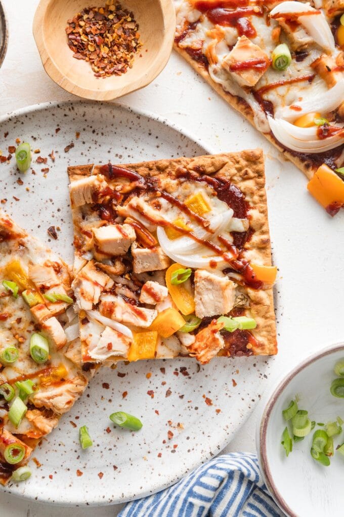 Close up of a BBQ chicken flatbread on a white plate.
