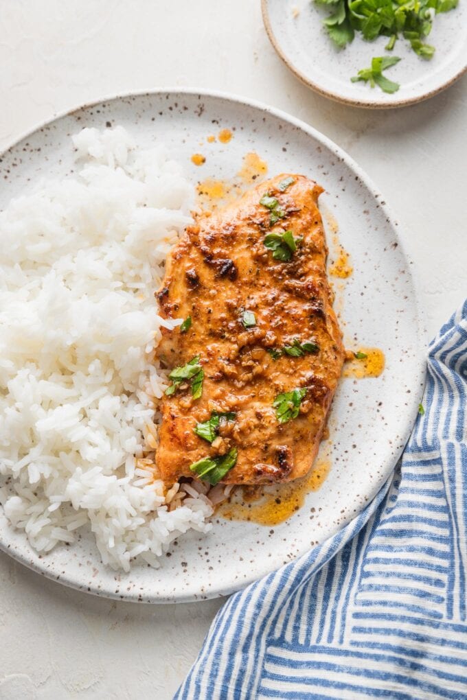 Cajun butter chicken breast with plenty of sauce, parsley for garnish, and a side of white rice on a white ceramic plate.