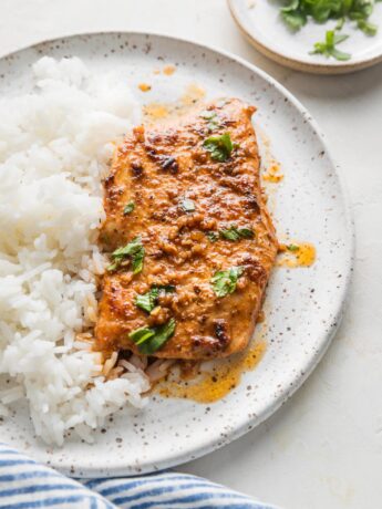 Cajun butter chicken breast with plenty of sauce, parsley for garnish, and a side of white rice on a white ceramic plate.