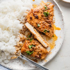 A thin-sliced chicken breast cooked with Cajun butter sauce and plated alongside white rice, with one slice cut to reveal a moist, tender interior.